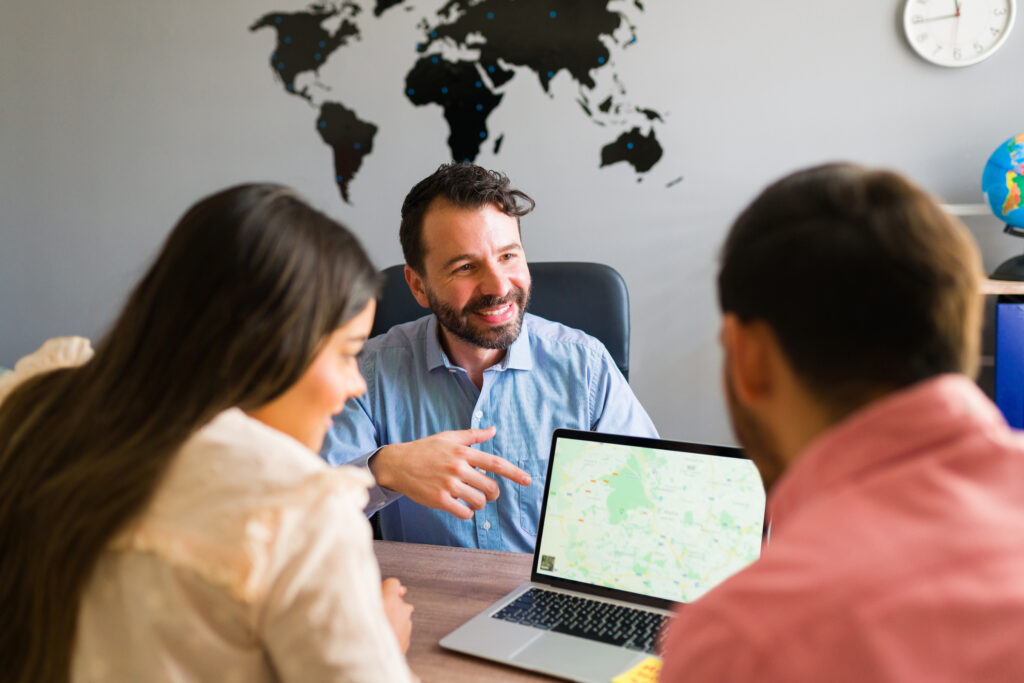 Here is your next trip destination. Rear view of a beautiful couple looking at a map on a laptop at the travel agency and choosing where to go on vacation